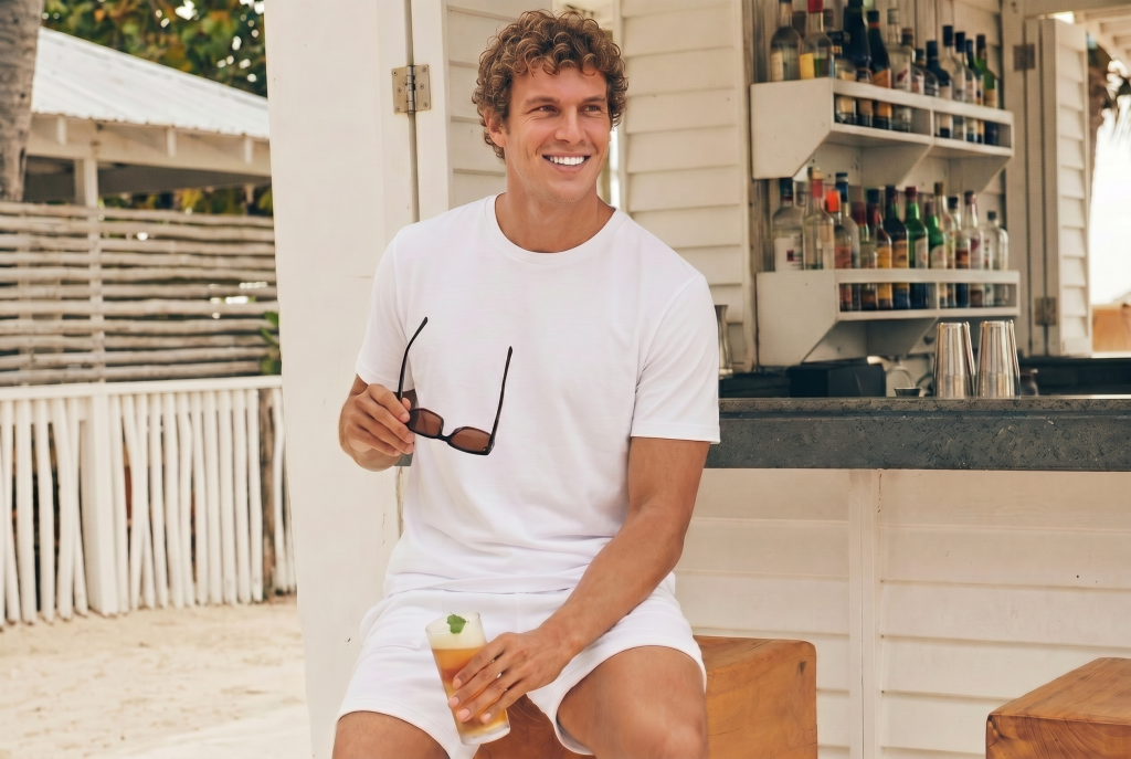 Man in alto relaxed tee from ten 10 apparel. He is relaxing at the beach with a drink and sunglasses in hand