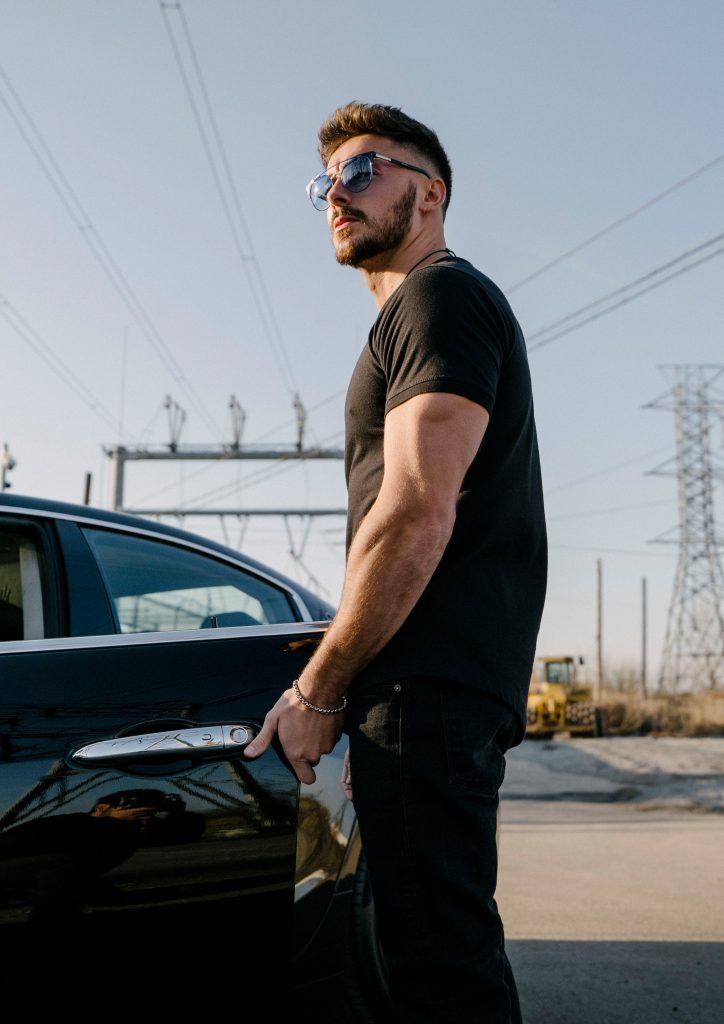 Male model in a black curved hem t-shirt standing next to sports car