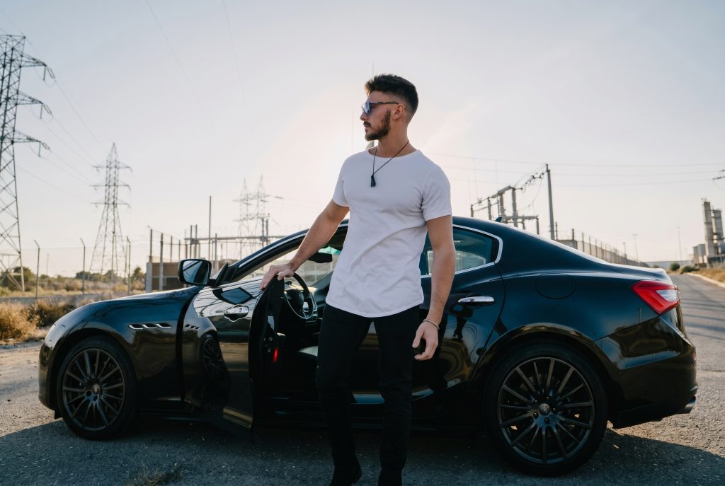 Man in Curved Hem white tee from Ten10 apparel with black sports car behind him