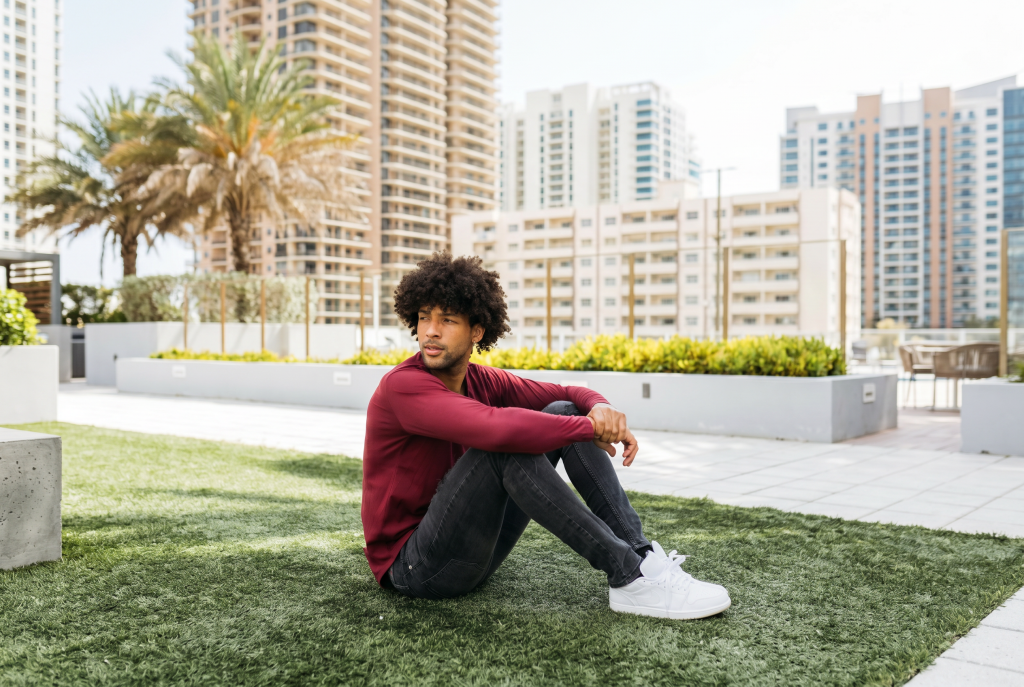 man wearing red long sleeve curved hem sitting down in the grass