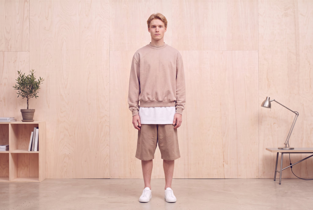 trendy outfits for men in 2026. Man wearing neutral sweater and white undershirt with shorts