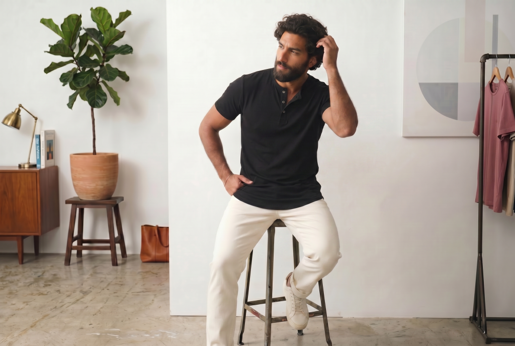 Man in a fitted black henley sitting on a stool from ten10 apparel