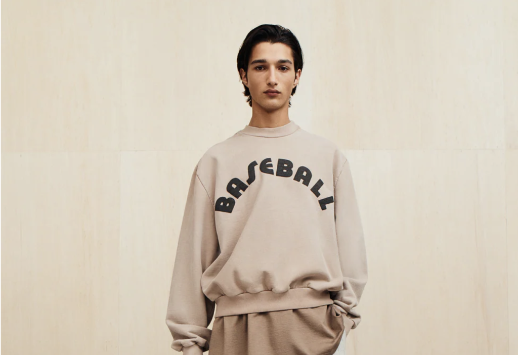 Man standing in neutral background with baseball lettered sweatshirt on